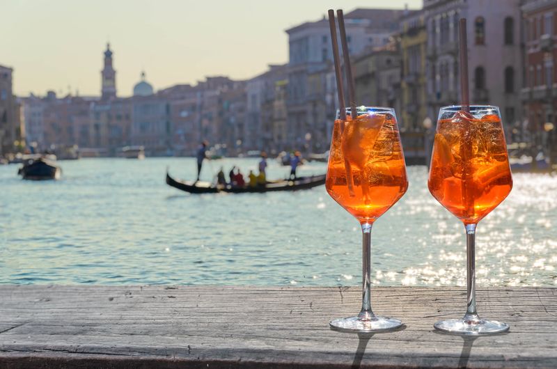 Nicht nur die Spritz-Varianten, auch das Original lässt sich in nur wenigen Schritten zu Hause mixen. Für einen echten Aperol Spritz nach dem italienischen Originalrezept nehmen Sie zwei Teile weißen Schaumwein (Prosecco frizzante) und einen Teil Aperol und vermische das Ganze mit einem Schuss Mineralwasser. Zum Schluss noch ein paar Eiswürfel hineingeben und mit einem Strohhalm genießen.